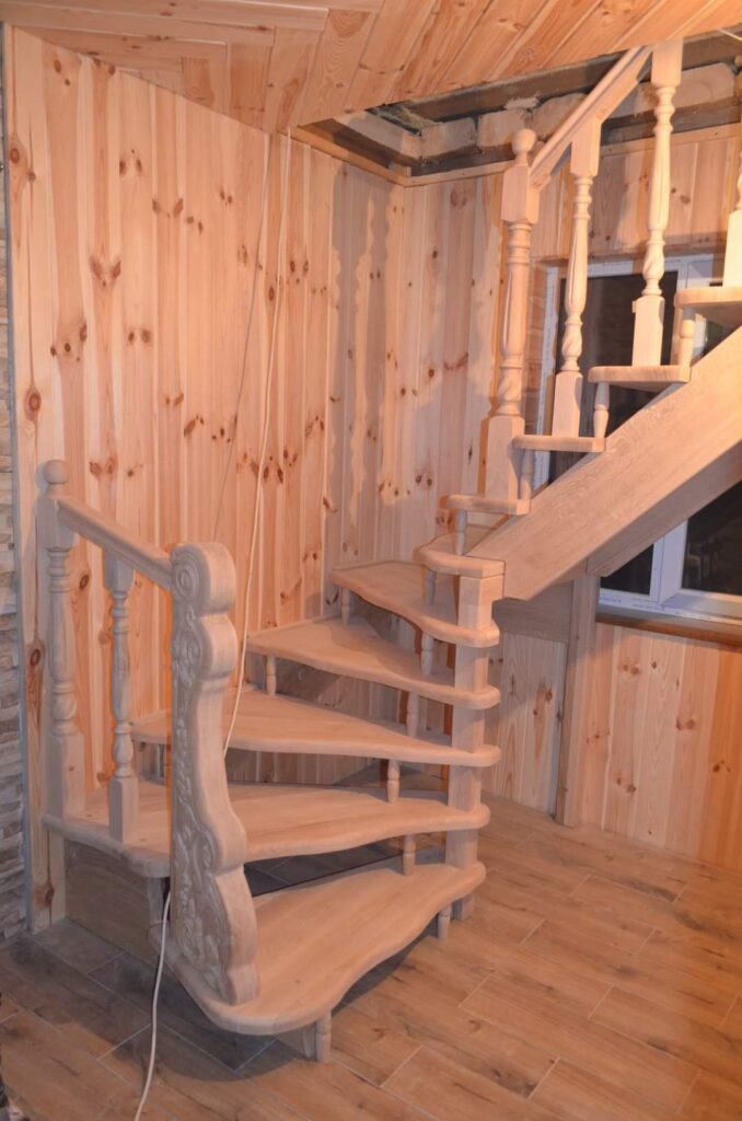 Zakrzywione schody drewniane we wnętrzu z wykończeniem z jasnego drewna; ściany i sufit również pokryte drewnianymi panelami, a na podłodze ułożone płytki ceramiczne.